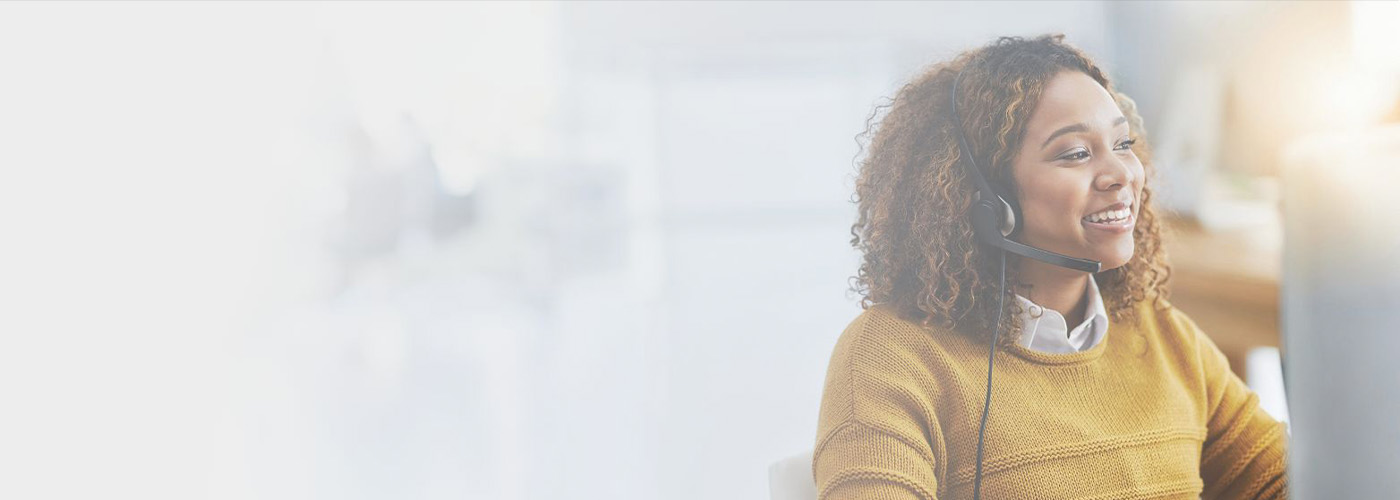 Female associate in yellow sweater wearing a black headset with microphone inside a call center
