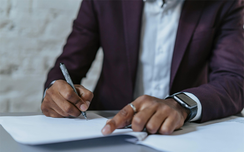 Person in suit jacket signing paper with fountain pen, torso visible only