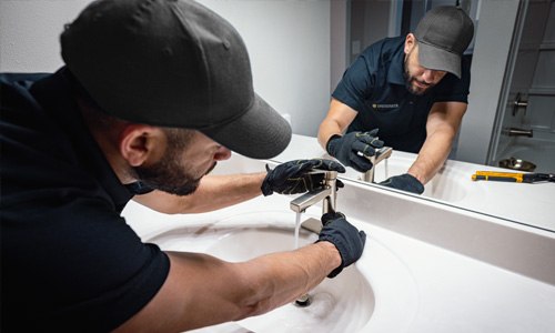 Maintenance professional installing a new silver faucet into a multifamily apartment's bathroom vanity over the sink.