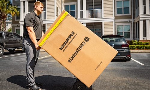 HD Supply RenovationsPlus Kitting delivery box on a hand truck being wheeled by HD Supply delivery driver across the parking lot of a multifamily housing complex.
