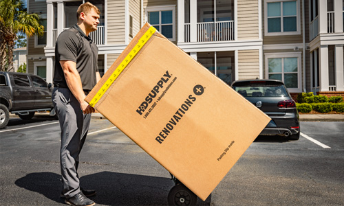 RenovationsPlus delivery man wheeling a kit exclusive packaging box across an apartment communities parking lot